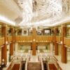 Luxurious hotel lobby with marble floor, wood columns, and a sparkling crystal chandelier overhead.