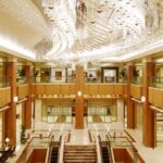 Luxurious hotel lobby with marble floor, wood columns, and a sparkling crystal chandelier overhead.