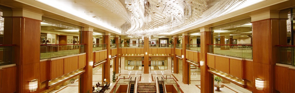 Luxurious hotel lobby with marble floor, wood columns, and a sparkling crystal chandelier overhead.