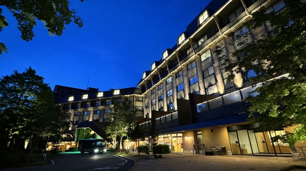 Exterior of a modern hotel at night, illuminated facade with trees along the curved driveway and entrance lights